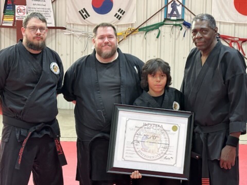JJ at a martial arts belt ceremony with instructors and a student